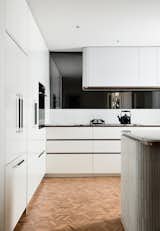The light and airy kitchen features a gently curved hood and island, which echo the design play throughout the house. Appliances by Fisher &amp; Paykel are hidden behind custom fronts for a clean and streamlined aesthetic in what is a functional, but compact, space.
