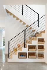 This family home in Tampa, Florida, includes an open-plan kitchen and living area with polished concrete floors, wooden accents, and crisp white walls. To eliminate clutter in the new-build, the team at Studio MM designed custom cubbies underneath the staircase, which feature light wooden baskets to match the extra-deep stair treads.
