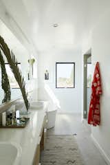 The main bathroom, with a prominently placed soaking tub, is a restorative haven within the home. "My favorite part [of the home] is the bathtub, which has a clerestory window of the downtown skyline, and another window that looks out to see the Hollywood sign in the distance," shares Melanie. The luminous space features ceramic floor tile from Ceramic Technics in Ecco Mineral Stone 2.0, Wilsonart quartz counters in Rio Upano, and a white LED sconce by StudioM. The white oak vanity was custom designed by OPEN For Humans.