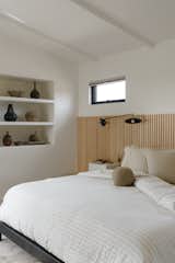 The vertical addition carved out new space for a main bedroom, bathroom, and walk-in closet. A slatted wood wall anchors the bed, adding texture and warmth to the couple's bedroom oasis, which is decorated with neutral, earthy tones.