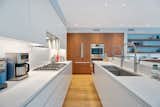 A mix of white in the kitchen - painted cabinets, soft white Caesarstone countertops, and a faux marble backsplash - are paired with custom natural walnut cabinetry to house the fridge, ovens, and pantry cabinets.