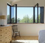 Glo European thermally broken aluminum dual-pane windows, shown here in the master bedroom, give the couple a corner view over the treetops without compromising the building envelope, and can be opened in a variety of configurations.  Photo 5 of 9 in Budget Breakdown: An Architect Couple Build a Net-Zero Home and Studio for $250 Per Square Foot