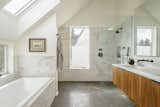 The upstairs master bathroom is teeming with light thanks to its skylight and windows, and looks more luxurious than it is thanks to marble-like ceramic tile and walnut-faced plywood cabinets.