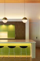 Pops of green lacquer-painted wood, gently spotlit to heighten their presence, are juxtaposed against walnut cabinetry and a poured-in-place terrazzo countertop.