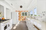 In the kitchen, which enjoys unobstructed views from the front of the house, the homeowners updated surfaces while adding bold-patterned wallpaper and flooring.