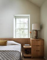 The custom headboard features built-in storage, with curved lines reminiscent of Shaker design. The bed linens are from Cultiver, the quilt is vintage, and the throw pillows are from Elitis, available from Assembly Line.