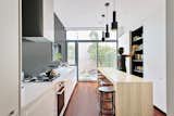 The long, narrow kitchen, at only 11 feet wide, is delineated by the ‘tapas bar’ island, a wall of floor to ceiling concealed cabinetry, and a long white counter contrasting with a charcoal wall.