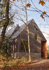 Natural materials were chosen to complement the rustic context. Greyed wood siding contrasts the natural cedar soffits and screen framing the entrance, sitting atop the raw, board-formed concrete base.