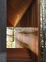 The slatted screen echoes the tree trunks seen through framed views at each end. The cedar slats are animated by the ever-changing west light that filters through its openings, producing a dynamic interplay of light and shadows.