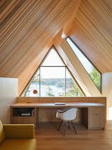 The split roof design features two intersecting gables that create opportunities for window openings where the roof volumes separate, seen at eye-level from the upper loft. A built-in desk features views down to the living space on the first level and the lake beyond.