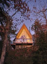 Tucked into the trees at the top of a steep slope, the Bunkie’s warm cedar interior lights up like a lantern in the evening.