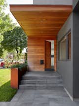 A cantilevered porch overhang, clad in warm cedar that wraps down the elevation and covers the front door, creates a bold and inviting entrance. The driveway’s granite pavers seamlessly transition onto the entrance porch, adding to the cohesive design.