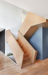 The monolithic stair guard’s diagonal wood grain imparts a sense of craftsmanship while also evoking a feeling of movement and energy. Walls painted in shades of grey-blue serve as further defining elements against the white walls and oak flooring.