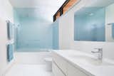 Blue finishes within the principal bathroom echo the materiality present in other areas of the house, while the contrast against the white millwork and flooring imparts a sense of water-like tranquility to the bathing areas.
