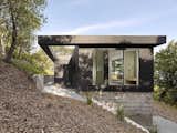 The wood-clad addition sits atop a concrete plinth which mediates the hillside.