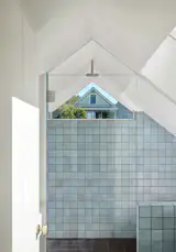 A hidden bath under the historic front gable has a perfectly framed view of the Victorian neighbor across the street.  The frameless glass wall makes this small space feel larger. Mottled blue tile from Heath Ceramics provide a rich and tactile surface.  Smoother gray floor tiles, also from Heath, are heated underneath. 