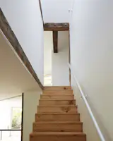 An anodized aluminum handrail and original exposed beams in the vaulted stairwell. The minimalist staircase is crafted from the farmhouse’s original wall planks.