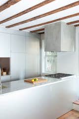Custom cabinetry in anodized aluminum, a concrete cube range hood, and Carrara marble countertops in the kitchen.