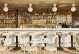 The bar area of Summerly, the rooftop bar and restaurant, displays brass stools upholstered with floral-patterned fabric, geometric tile, and cafe tables and chairs. 