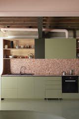 After: Pink-toned terrazzo tile counters and a backsplash and olive green-painted cabinetry enlivens the kitchen, where the designers created open shelving using leftover plywood from the mezzanine ceiling panels.