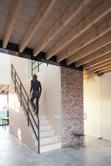 A birch staircase features extensive storage and contrasts with the concrete floors and the reclaimed brick of the partial wall. The wire stool was designed by Cees Brakman and the ceiling beams are made from pine.