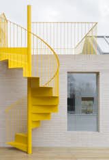 The sunshine-yellow spiral staircase stands out against the pale tone of the brick facade.