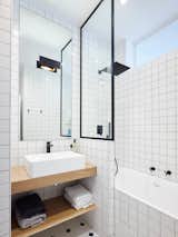 Bath, Wood, Ceiling, Porcelain Tile, Porcelain Tile, Wall, Corner, Alcove, and Vessel To add balance and interest, the architect contrasted the texture of oak shelving with the sleek finish of glossy white tile in the bathroom.   Bath Corner Vessel Alcove Ceiling Photos from Budget Breakdown: A Muddled Parisian Pad Gets a Sleek Makeover for $117K