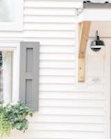 Window shutters, planted window boxes, white-painted cedar siding, and an industrial-style metal sconce enliven the exterior the farmhouse-style tiny home.