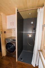 The bathroom is accessed via a partition door with a full-length mirror. The room also features a sizable shower, a dry toilet with a stainless-steel bucket and chip compartment, a large wardrobe, and a washing machine.