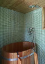 Brilliant green mosaic tile covers the walls and the floor of the bathroom, where the architects arranged a varnished wood soaking tub.
