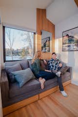 Heather and Kevin sit on a custom sofa in the living room, which features a bank of drawers underneath for storage. Above, a WarmlyYours mirror emits radiant heat and helps warm the tiny home.