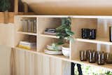 The kitchen’s plywood open shelving is stacked with ceramic plates and bowls, cups, and drinking glasses made from recycled glass.