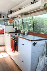 Kitchen, Wood Counter, Undermount Sink, Drop In Sink, White Cabinet, Cooktops, and Medium Hardwood Floor The kitchen showcases wood counters and white-painted cabinetry.  Photo 5 of 20 in An Australian Couple Turn a Bus Into a Traveling Tiny Home and Physical Therapy Practice