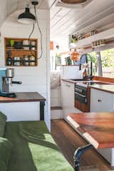 Kitchen, Refrigerator, Wood Counter, Drop In Sink, Undermount Sink, Medium Hardwood Floor, White Cabinet, and Cooktops A flip down side table and a built-in sofa in the living area provide a place to sit and drink morning coffee.  Photo 6 of 20 in An Australian Couple Turn a Bus Into a Traveling Tiny Home and Physical Therapy Practice