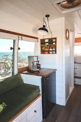 Living Room, Bench, Ceiling Lighting, Sofa, and Medium Hardwood Floor A small refrigerator beneath the coffee counter allows the couple to store all the food and drinks they need while traveling and working.  Photo 9 of 20 in An Australian Couple Turn a Bus Into a Traveling Tiny Home and Physical Therapy Practice