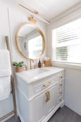 In the bathroom, a round mirror with a wood frame, mounted on ceramic wall tile, hangs above a white-painted vanity with brass pulls. "We design our bathrooms to be airy, light, and luxurious," Elizabeth says.