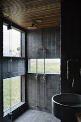 Volcanic bluestone tile, exposed copper pipes, and a slatted timber ceiling provide a textured and moody feeling in the bathroom.