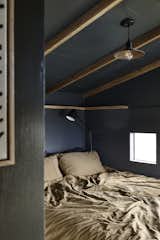 In the lofted sleeping area, small, square windows on either side of the bed let in views of the landscape.