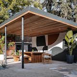 The designers recreated the carport as a dining area, arranging the space with a living wall, a painted brick wall, a tk ceiling with recessed lighting, a teak table and bench, and director chairs.