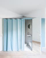 The bathroom, adjacent to the kitchen, features a pale blue exterior wall that ties it to the kitchen area. A mirrored panel on the inside of the door reflects space and light, creating a feeling of spaciousness.