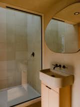 An oblong mirror hangs above the vanity in the bathroom. The shower is finished in tile from Stone Source.