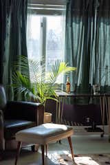 The upstairs den has a moodier feel with dark-purple walls, sheer green drapery, and a vintage bar cart.