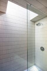 A skylight in the primary bathroom floods the space, tiled with bright white ceramic tile, with soft sunlight.