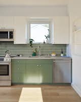 The kitchen is adorned with Fireclay olive-green tile on the backsplash that ties to the green-painted custom millwork of the lower cabinetry.