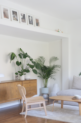 Plants, an upholstered sofa, and a wood console, chair, and coffee table supply warmth and texture in the understated living area.