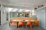 An integrated oak bench with storage bridges the kitchen and the dining area, where a massive oak table is surrounded by orange dining chairs.