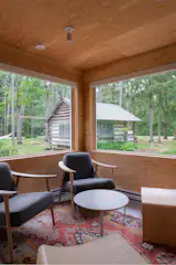 An original 1800s log cabin serves as an office space for the property and is viewed from the living area, where a vibrant vintage rug supplies color and pattern.