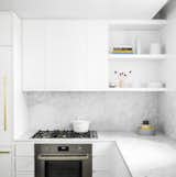 The white minimalist kitchen is fully outfitted with premium Bertazzoni Italia and Bosch appliances. It also features Italian Cararra marble countertops, an island, custom-designed cabinetry, and natural brass Fantini fixtures.&nbsp;