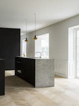 The minimalist kitchen in smoked oak with bronzed brass handles was designed by Norm Architects for the Danish kitchen manufacturer Reform, and is complemented by a sculptural kitchen island in a light gray ceramic stone, as well as a herringbone floor.