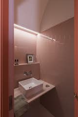 Bath Room, Tile Counter, Porcelain Tile Wall, Vessel Sink, and Accent Lighting The guest bathroom sits hidden in a coral-colored arch volume off the kitchen.  Photo 22 of 26 in Before & After: An Ancient Barcelona Apartment Gets a Colorful, Chic Makeover
